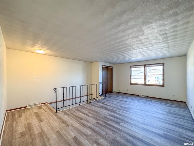 unfurnished room featuring visible vents, a textured ceiling, baseboards, and wood finished floors