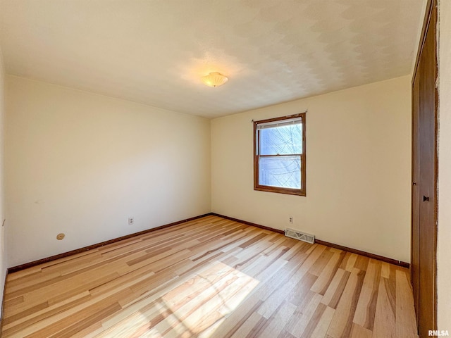 spare room featuring light wood-style flooring, visible vents, and baseboards