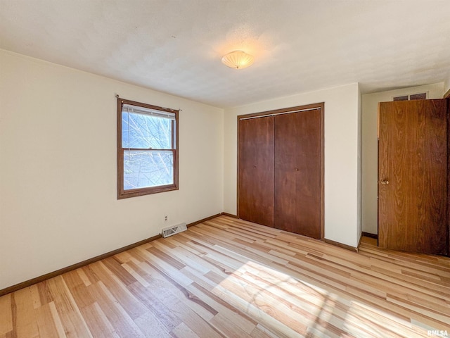 unfurnished bedroom with light wood-type flooring, a closet, visible vents, and baseboards