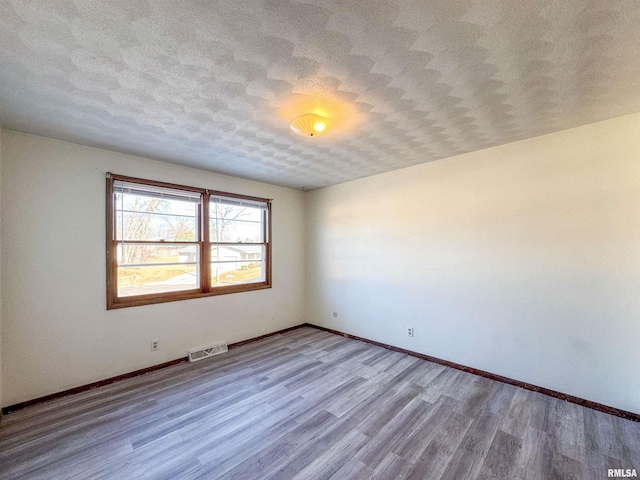 empty room with baseboards, a textured ceiling, visible vents, and wood finished floors