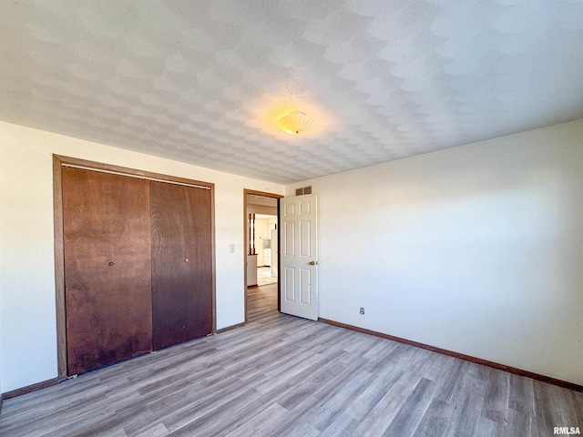 unfurnished bedroom with light hardwood / wood-style flooring, a closet, and a textured ceiling