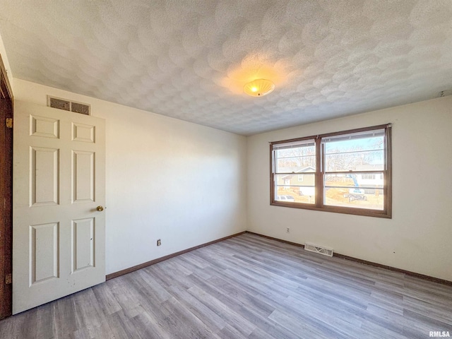 unfurnished room with a textured ceiling, wood finished floors, visible vents, and baseboards