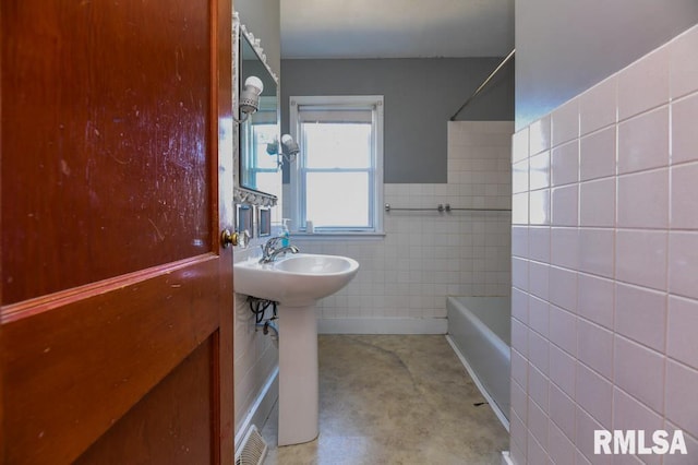 bathroom with a tub, sink, and tile walls