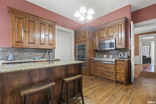 kitchen with stainless steel appliances, light stone countertops, dark hardwood / wood-style flooring, and decorative light fixtures