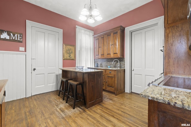 kitchen with pendant lighting, a breakfast bar area, dark hardwood / wood-style floors, light stone counters, and a notable chandelier