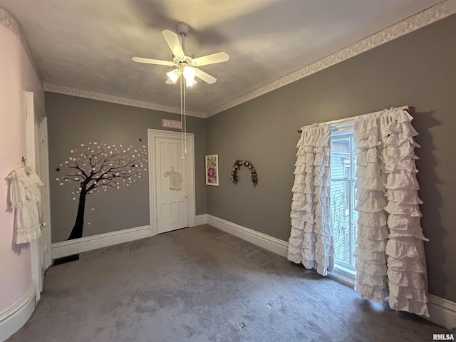 empty room featuring crown molding, dark carpet, and ceiling fan