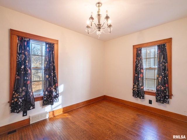 spare room featuring wood-type flooring and a chandelier