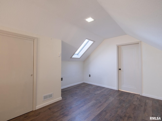 bonus room featuring dark wood-type flooring, vaulted ceiling with skylight, and a textured ceiling