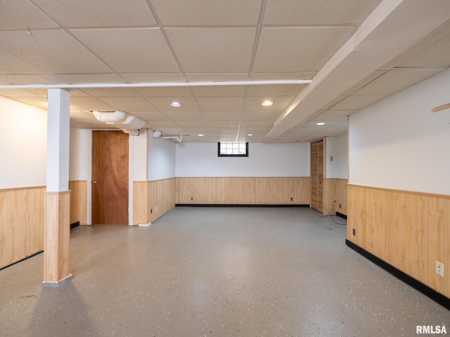 basement with a drop ceiling and wooden walls