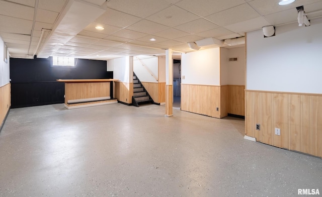 basement with a paneled ceiling and wood walls