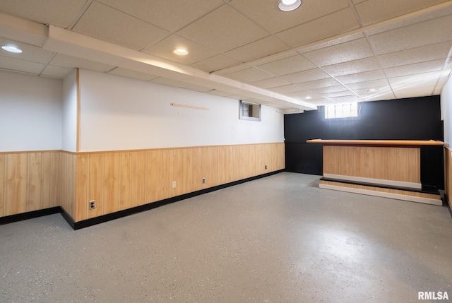 basement featuring a drop ceiling and wood walls