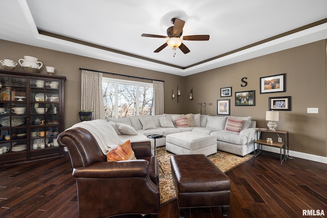 living area featuring dark wood-type flooring, a tray ceiling, ceiling fan, and baseboards