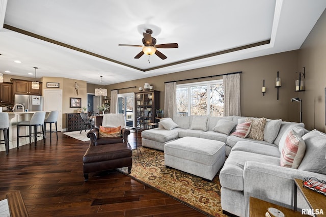 living area featuring ceiling fan, a tray ceiling, and dark wood finished floors