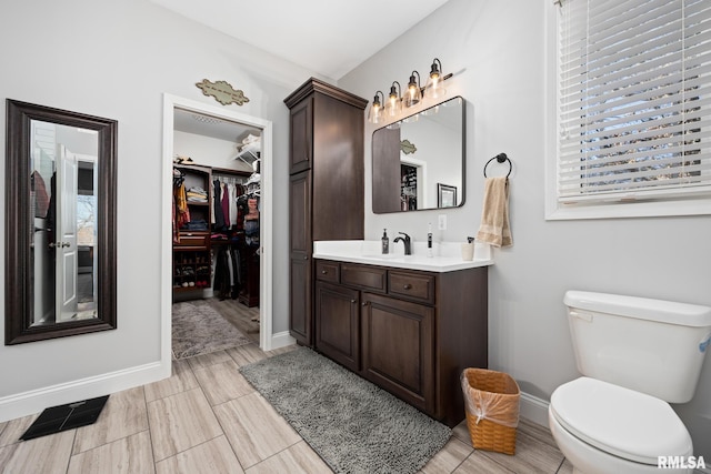 bathroom featuring toilet, vanity, visible vents, baseboards, and a walk in closet