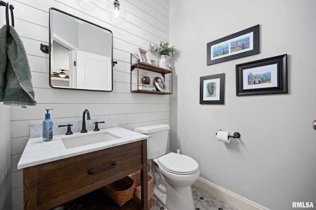 half bath with baseboards, wood walls, vanity, and toilet