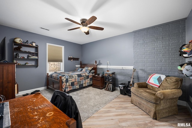 bedroom with a wainscoted wall, light wood-style flooring, visible vents, and ceiling fan