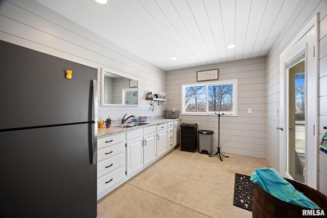 kitchen with light stone counters, freestanding refrigerator, white cabinetry, open shelves, and a sink