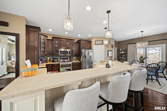 kitchen with glass insert cabinets, appliances with stainless steel finishes, light countertops, dark brown cabinets, and pendant lighting