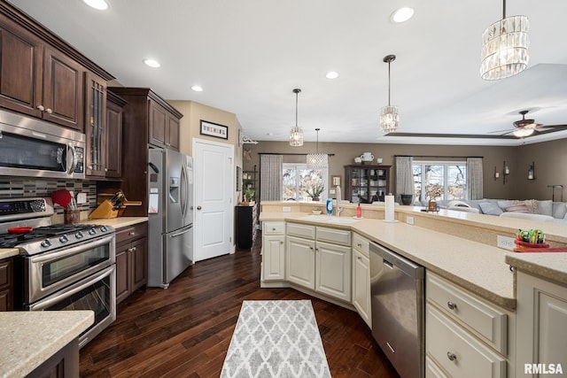 kitchen featuring cream cabinets, dark brown cabinetry, stainless steel appliances, open floor plan, and light countertops