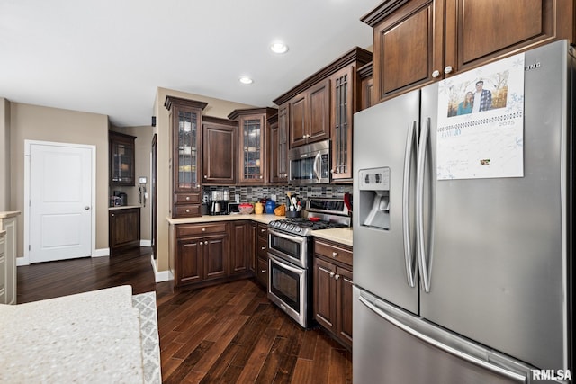 kitchen with tasteful backsplash, glass insert cabinets, appliances with stainless steel finishes, dark wood-style flooring, and light countertops