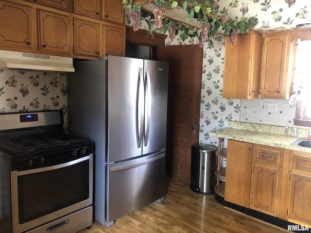 kitchen with sink, decorative backsplash, light wood-type flooring, and appliances with stainless steel finishes