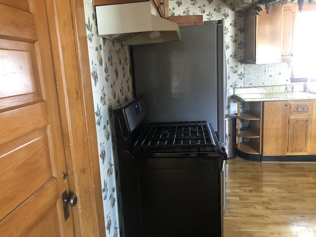 kitchen with ventilation hood, tasteful backsplash, gas range oven, and light hardwood / wood-style floors