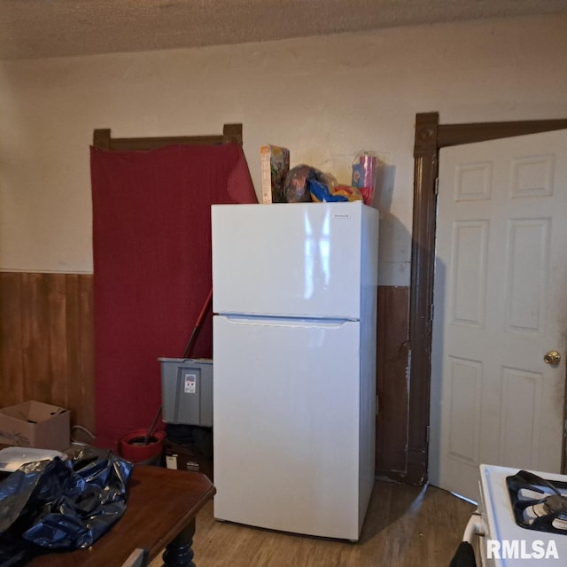 kitchen with white refrigerator, wooden walls, and light hardwood / wood-style floors