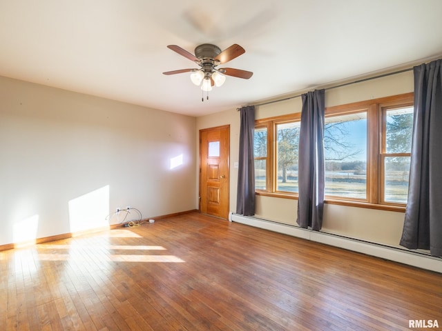 empty room featuring baseboard heating, ceiling fan, hardwood / wood-style floors, and a wealth of natural light