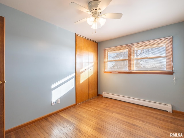 unfurnished bedroom featuring a closet, a baseboard heating unit, ceiling fan, and light hardwood / wood-style flooring