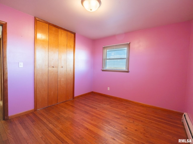 unfurnished bedroom featuring wood-type flooring, baseboard heating, and a closet