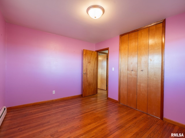 unfurnished bedroom featuring wood-type flooring, a baseboard radiator, and a closet