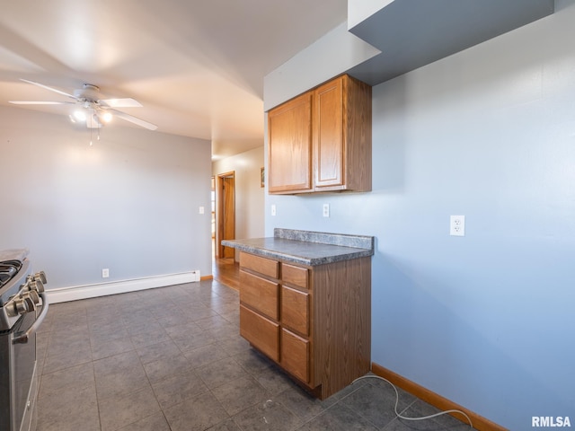 kitchen with stainless steel gas range oven, ceiling fan, baseboard heating, and dark tile patterned flooring