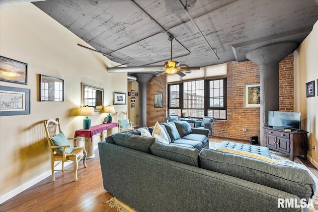 living room with ceiling fan, light hardwood / wood-style flooring, brick wall, and a wood stove