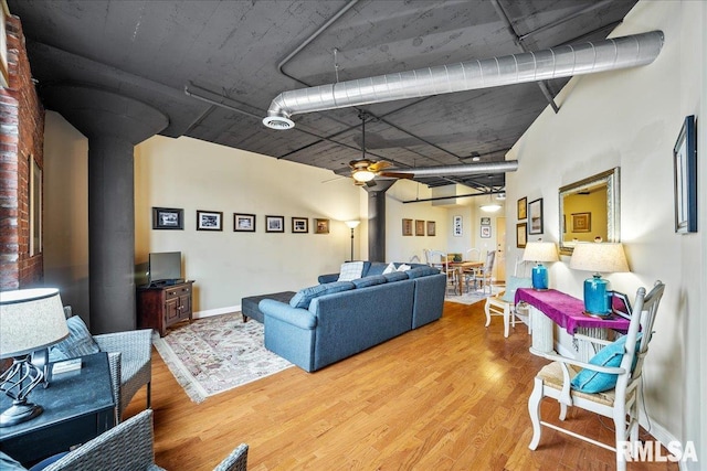 living room with wood-type flooring, a wood stove, and ceiling fan