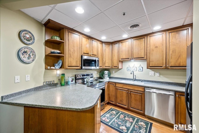 kitchen featuring stainless steel appliances, kitchen peninsula, sink, and light wood-type flooring