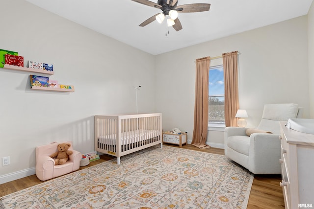 bedroom featuring ceiling fan, light hardwood / wood-style floors, and a crib