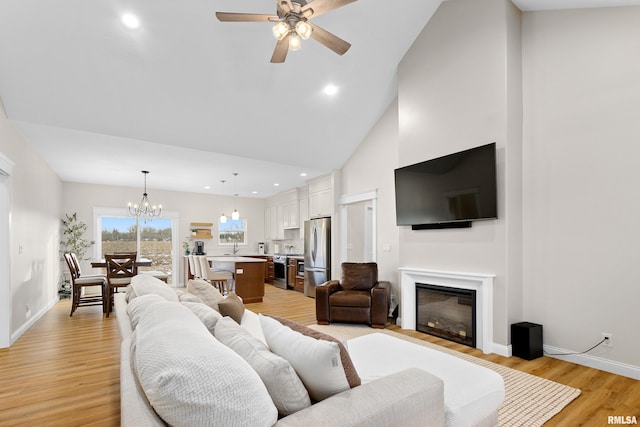 living room featuring ceiling fan with notable chandelier, high vaulted ceiling, and light wood-type flooring