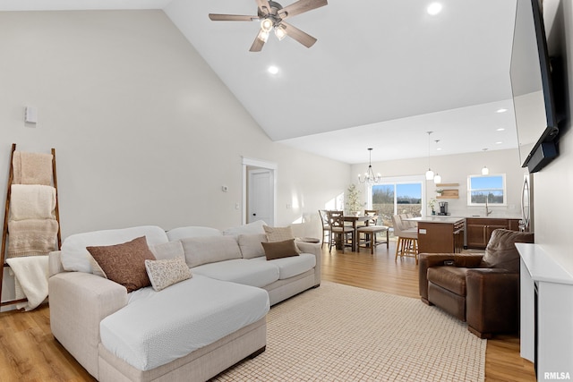 living room featuring ceiling fan with notable chandelier, high vaulted ceiling, sink, and light hardwood / wood-style floors