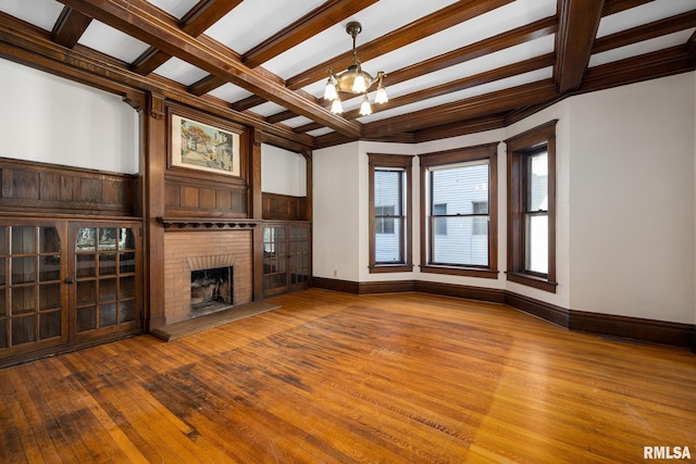 unfurnished living room featuring coffered ceiling, a chandelier, a brick fireplace, beam ceiling, and hardwood / wood-style floors