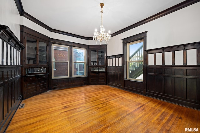 unfurnished dining area with crown molding, a chandelier, and light wood-type flooring