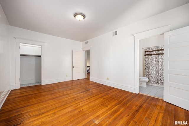 unfurnished bedroom with hardwood / wood-style flooring, ensuite bathroom, and a closet