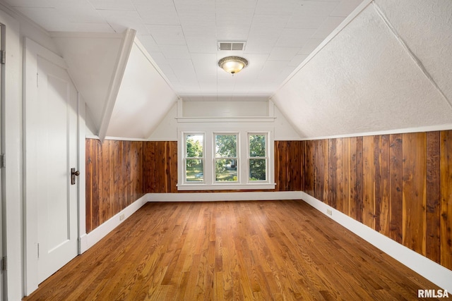 bonus room featuring lofted ceiling, hardwood / wood-style flooring, and wooden walls