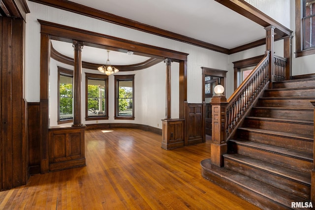 interior space featuring ornate columns, crown molding, hardwood / wood-style flooring, and a notable chandelier