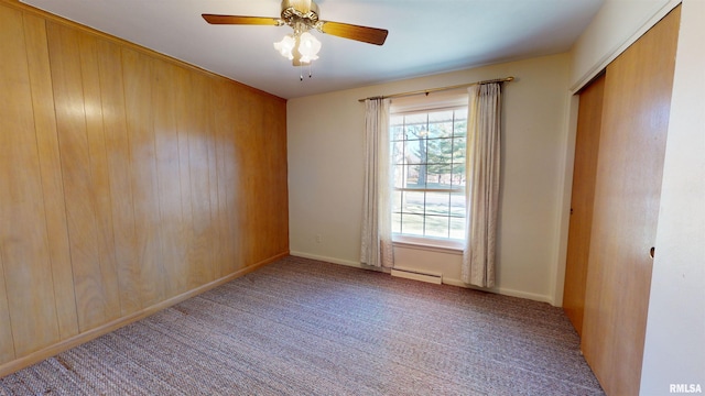 unfurnished room with baseboard heating, ceiling fan, wooden walls, and carpet floors