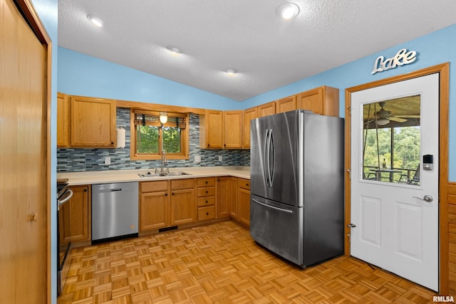 kitchen with lofted ceiling, sink, light parquet floors, appliances with stainless steel finishes, and a textured ceiling