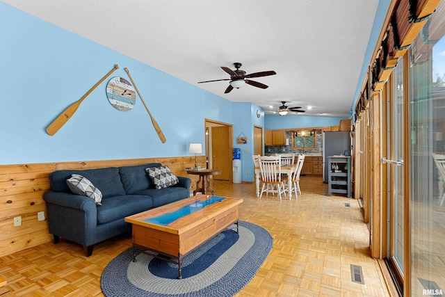 living room featuring lofted ceiling, light parquet floors, wooden walls, and a textured ceiling