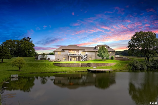 back house at dusk featuring a deck with water view and a lawn