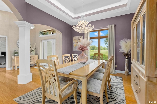 dining area featuring decorative columns, a chandelier, light hardwood / wood-style floors, and a tray ceiling