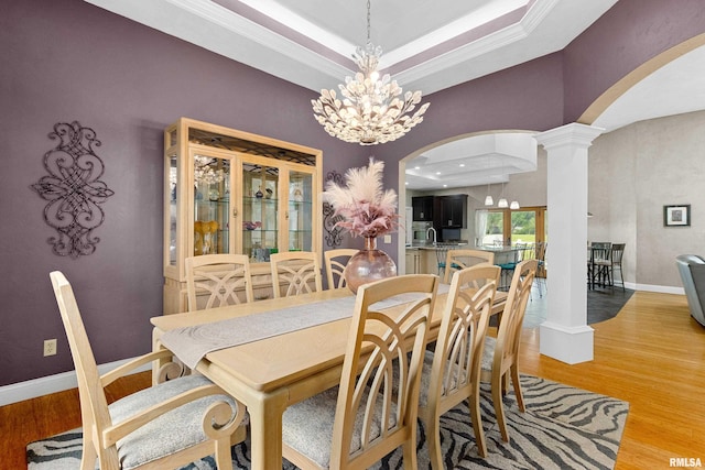 dining room featuring a notable chandelier, hardwood / wood-style flooring, ornamental molding, and ornate columns