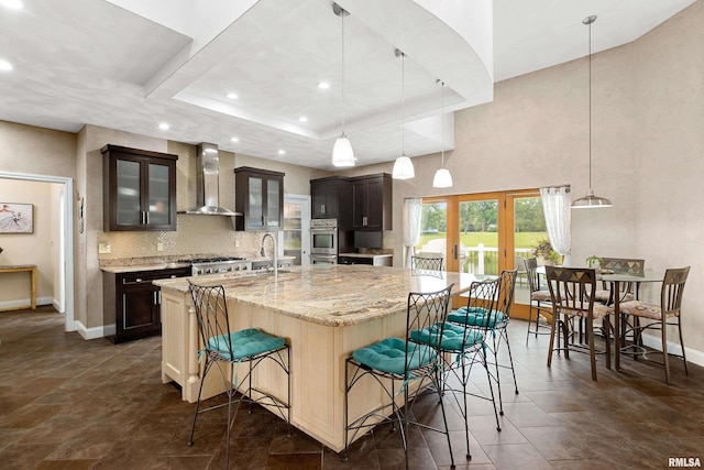 kitchen featuring a large island, decorative light fixtures, dark brown cabinets, and wall chimney exhaust hood